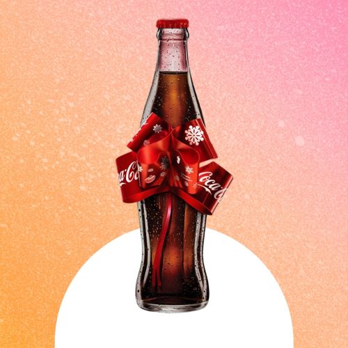 Coca-Cola glass bottle with a red ribbon shaped like a bow around the center, presented on a warm gradient background for a festive look.